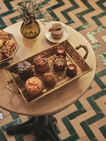 High-angle shot of an ornate gold tray with assorted pastries, a cup of coffee, and a vase with flowers on a marble table.