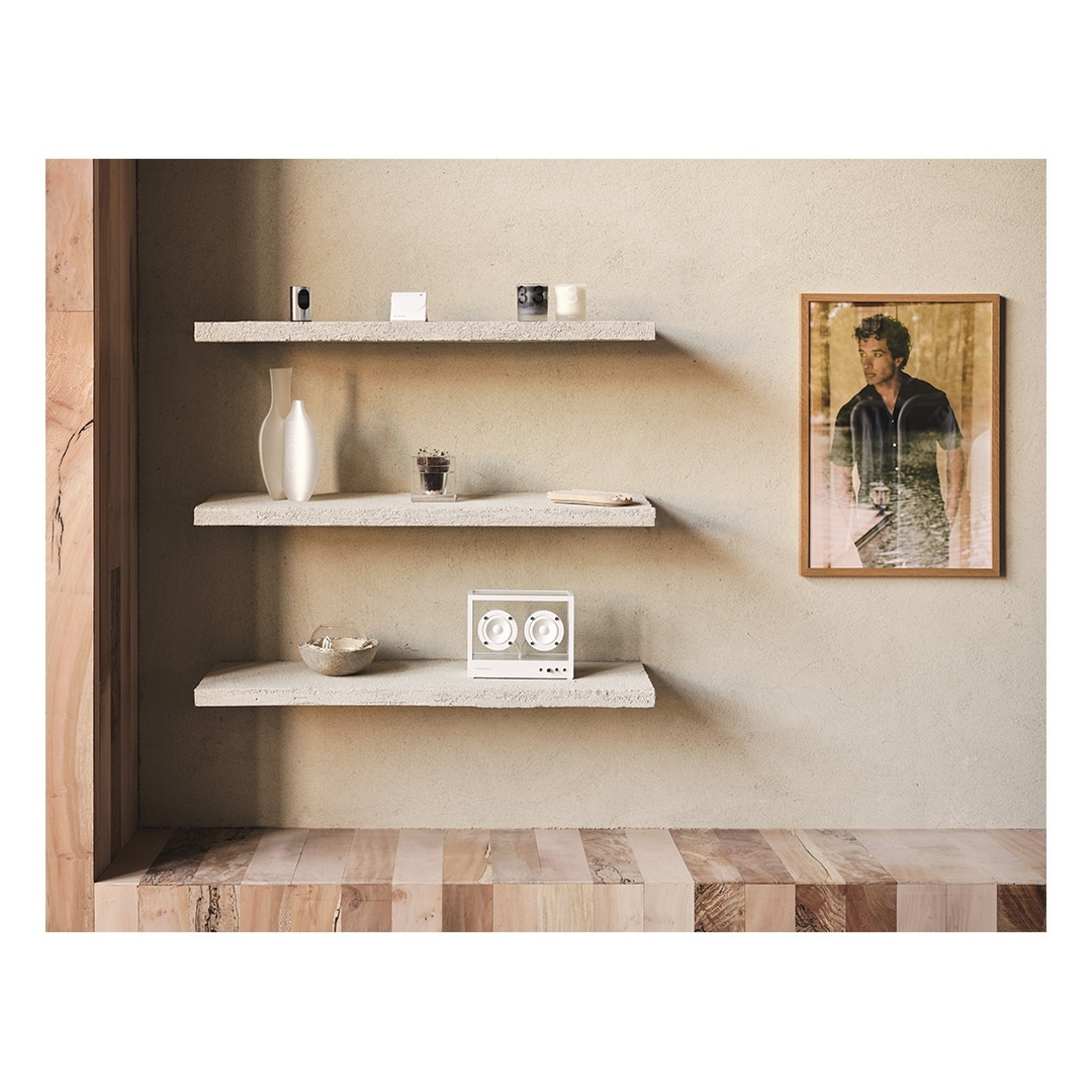 Interior setting with floating shelves displaying decorative items, including a speaker, vase, picture frame, and wooden floor.