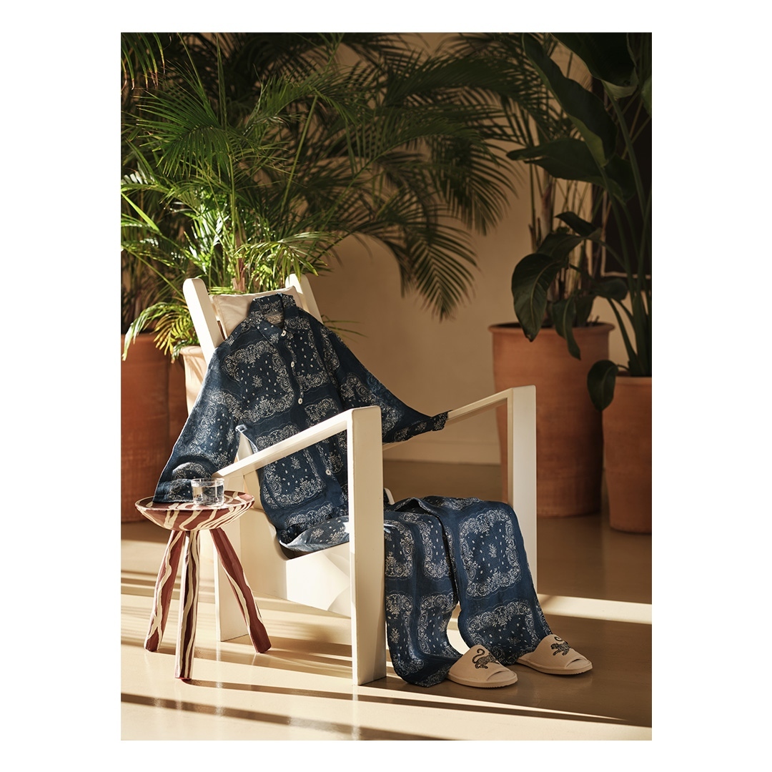 Indoor scene showcasing a paisley-patterned blue pajama set draped over a white armchair next to a small table with drinking glasses.