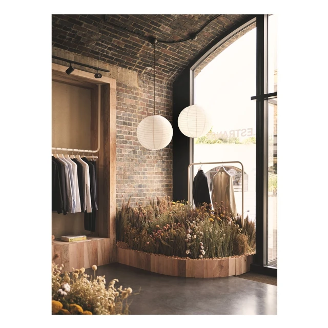 Interior view of a modern boutique with brick walls, clothes racks, and a circular display of dried flowers and paper lanterns.