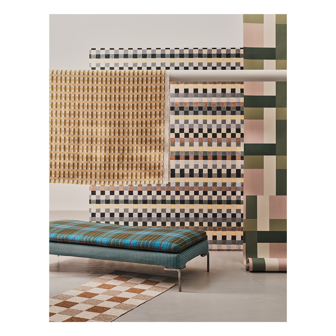 Interior studio shot of a modern geometric-patterned bench and matching rugs against a backdrop of patterned wallpaper rolls.