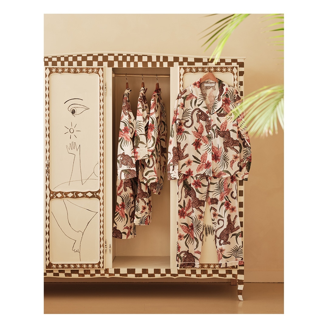 Pajama sets hanging in an ornate wardrobe featuring animal and floral patterns and hand-drawn art details on the doors.