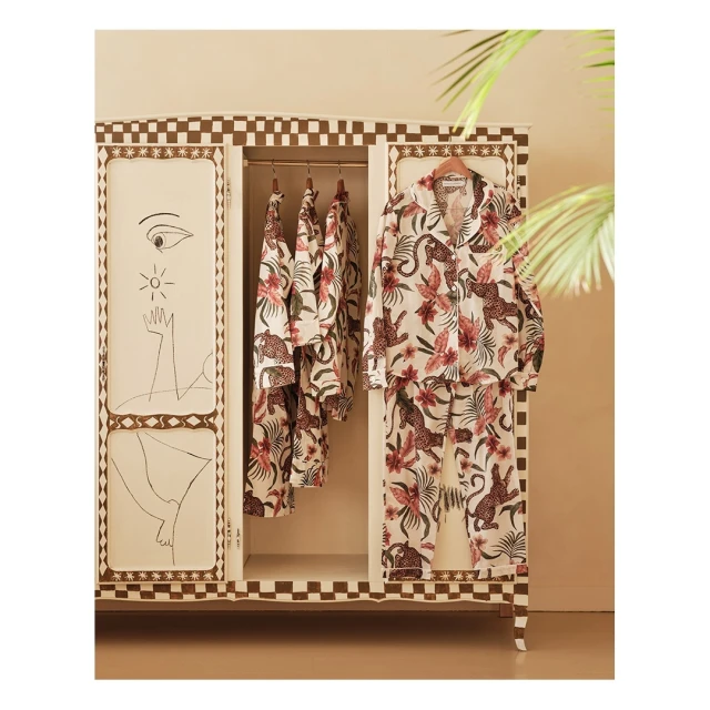 Pajama sets hanging in an ornate wardrobe featuring animal and floral patterns and hand-drawn art details on the doors.