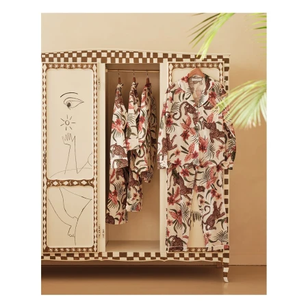 Pajama sets hanging in an ornate wardrobe featuring animal and floral patterns and hand-drawn art details on the doors.