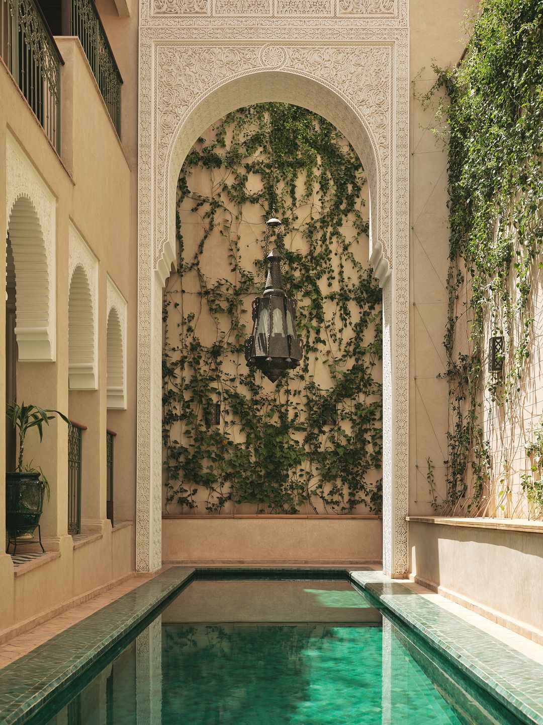 An ornate archway frames a swimming pool at a luxury hotel or resort. Lush greenery and traditional architecture create a serene atmosphere.