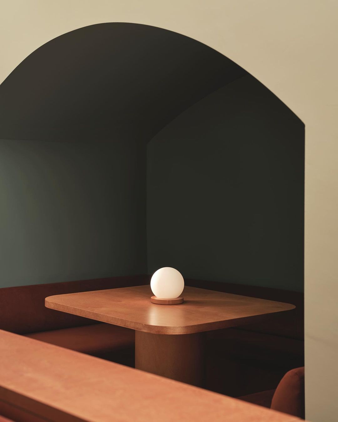Interior shot of booth seating in a restaurant with a wooden table illuminated by a spherical table lamp, showcasing contemporary design.