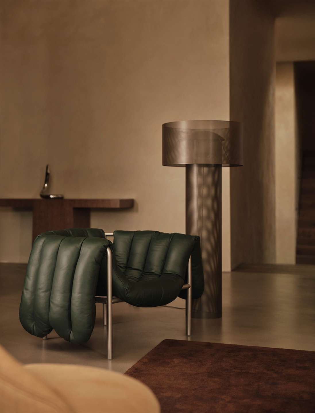 Indoor scene showcases an emerald green leather lounge chair with a silver frame, complemented by a wooden side table, a floor lamp, and a brown rug.