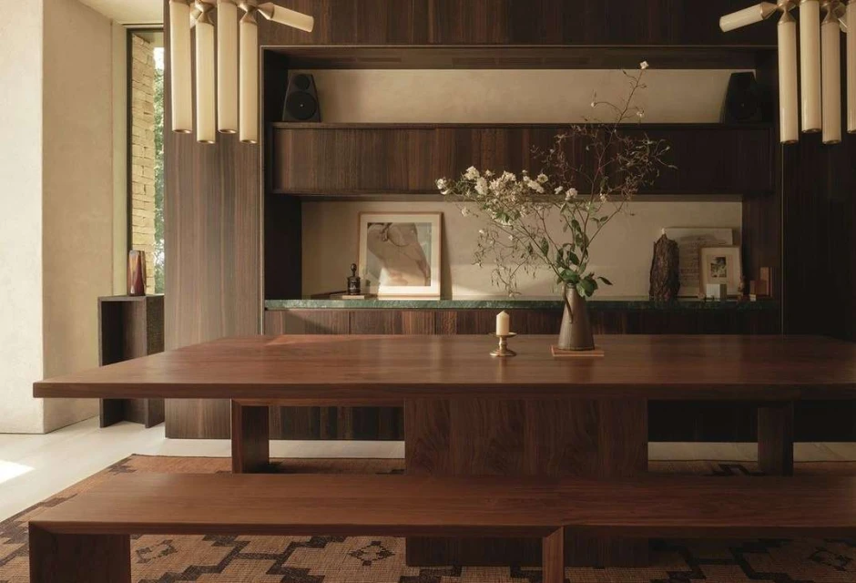 Interior of a dining room with a large wooden table, bench seating, floral centerpiece, and contemporary lighting fixtures. Warm and inviting.