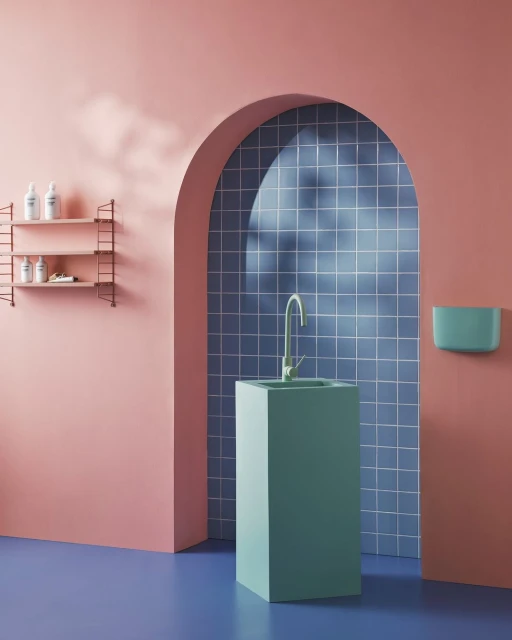 Minimalist interior with a light green pedestal sink and metal faucet set against a pink wall with a blue tiled archway.