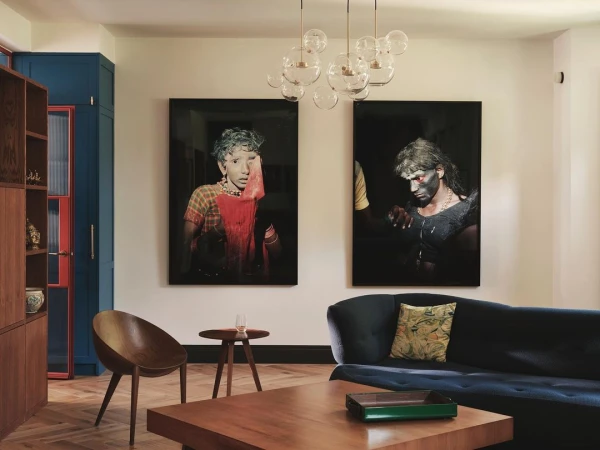 Living room interior with modern decor, featuring two large art portraits, a blue velvet sofa, hardwood floors, and a unique bubble chandelier.