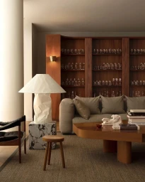 Modern living room interior with a large white sculptural lamp on a marble plinth, wooden coffee table, and built-in wooden shelving.