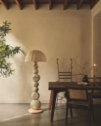 Tall decorative floor lamp with a patterned stacked-sphere base and beige domed shade in a warm minimalist room interior