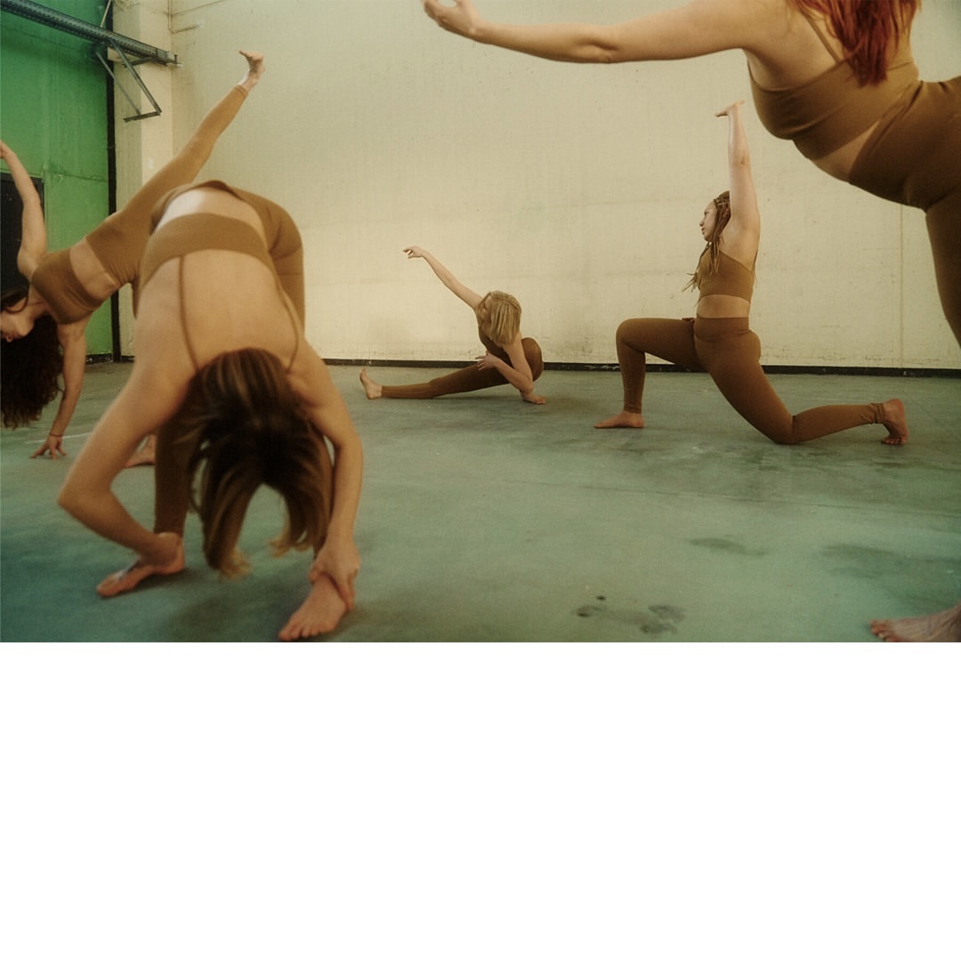 Group of women in athletic wear in various yoga poses in a studio with a green door and off-white walls on a concrete floor.