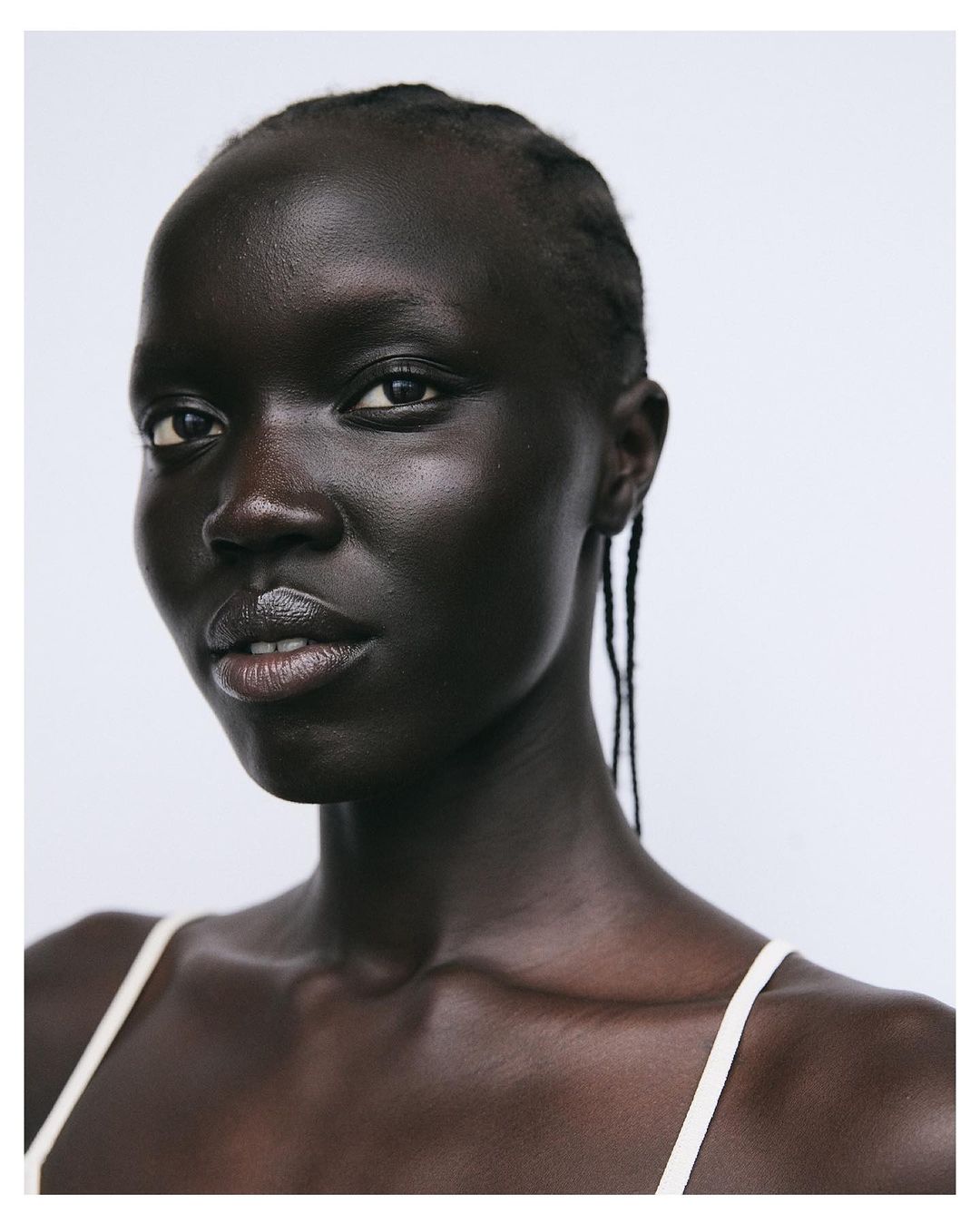 Close-up portrait of a Black adult female with neutral expression, wearing a neutral-colored top against a plain white background.