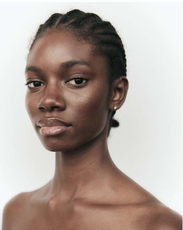 Portrait of a Black woman with braided hair and stud earrings against a neutral white background