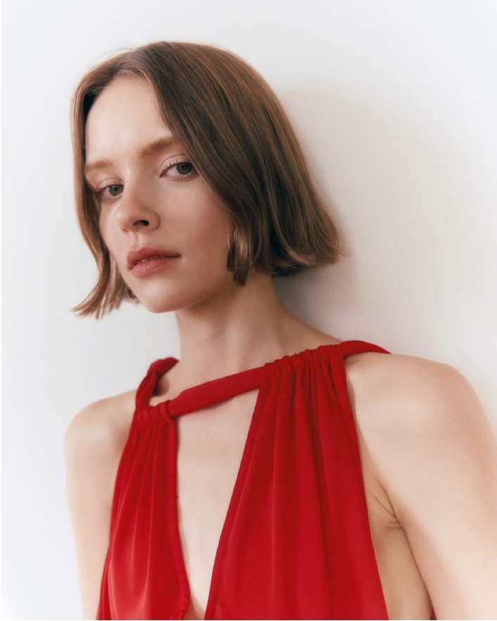 Close-up of a young woman in a red dress, posing in a photo studio. The image features a soft, diffused lighting.