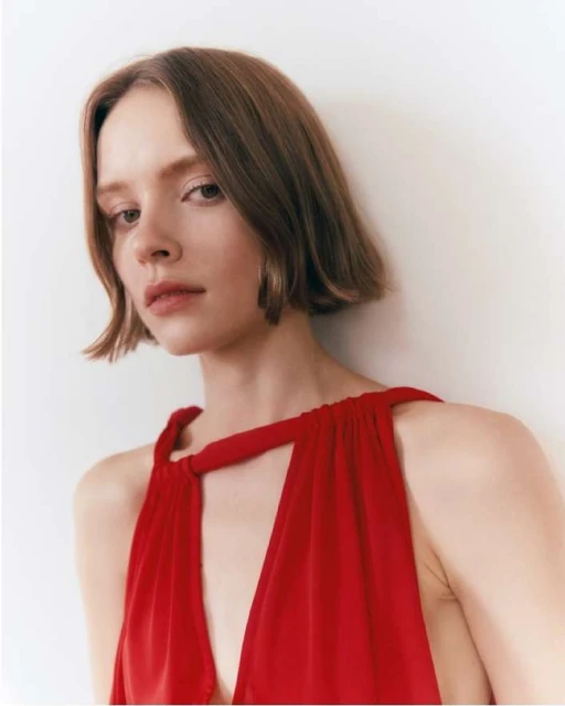 Close-up of a young woman in a red dress, posing in a photo studio. The image features a soft, diffused lighting.