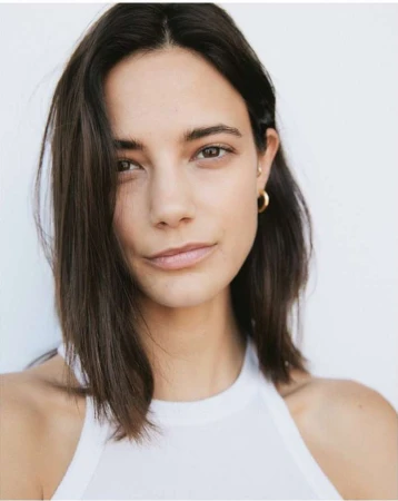 Close-up portrait of a woman with dark shoulder-length hair wearing a white tank top against a plain white background.