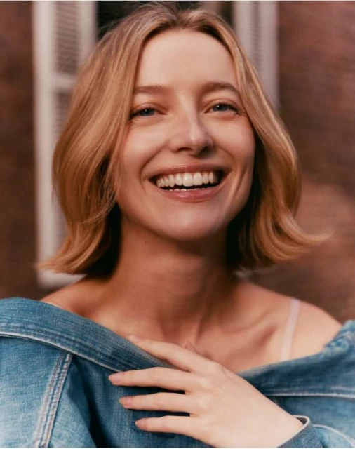 Close-up portrait of a blonde woman with a bright, wide smile wearing a denim jacket, showcasing a joyful and natural expression.