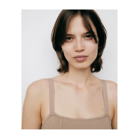 Portrait of a woman with dark hair and fringe wearing a beige tank top against a plain white background