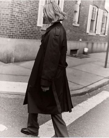Woman in a long dark trench coat walking across a city street, captured in black and white photography by Felix Wong.