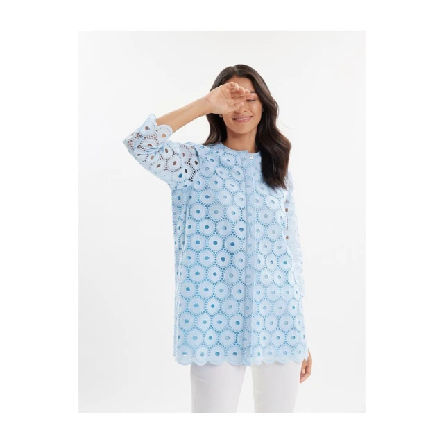 Fashionable adult female poses in an eye-catching baby blue tunic top with intricate circle cutouts, styled with white pants.