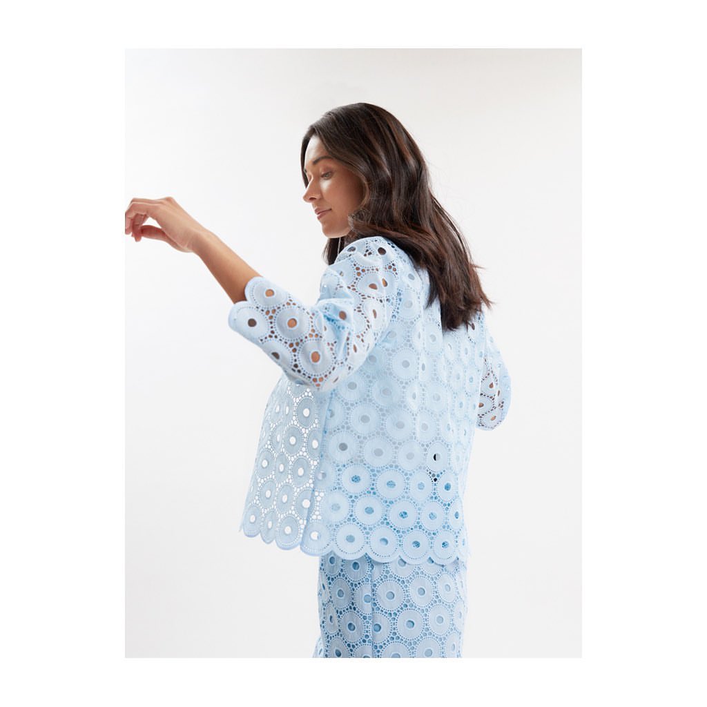 Woman wearing a light blue patterned eyelet lace top and matching skirt against a white background