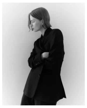 Model in a black blazer with crossed arms posing against a neutral studio background by photographer Felix Wong
