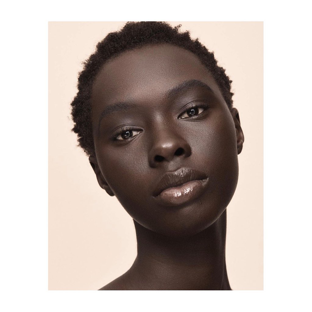 Close-up studio portrait of an African American woman with glossy lips against a neutral beige background, emphasizing beauty and skincare.