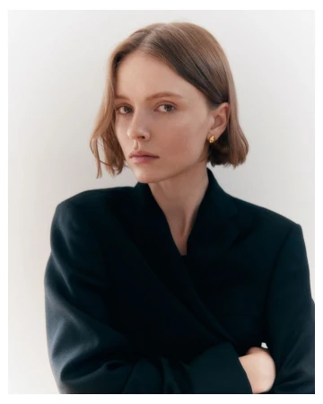 Portrait of a woman with short brown hair wearing a dark blazer against a plain neutral background.