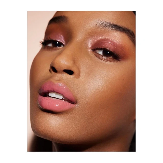 Close-up of a young woman with brown skin, glossy pink lips, and pink eyeshadow, showcasing beauty and makeup artistry.