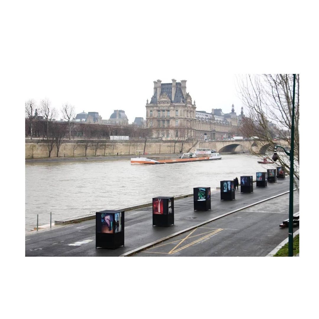 Seine river embankment in Paris with art installations. Buildings and river transport are visible in the background on an overcast day.