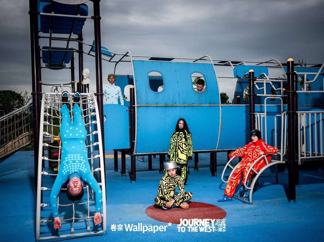 Editorial fashion shot featuring six models in colorful, patterned clothing on a playground with a jungle gym and cloudy sky.