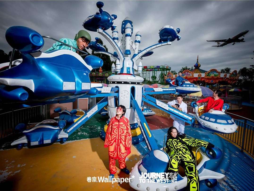 Group of people wearing colorful outfits on a rocket-shaped carousel ride at an outdoor amusement park under an overcast sky.
