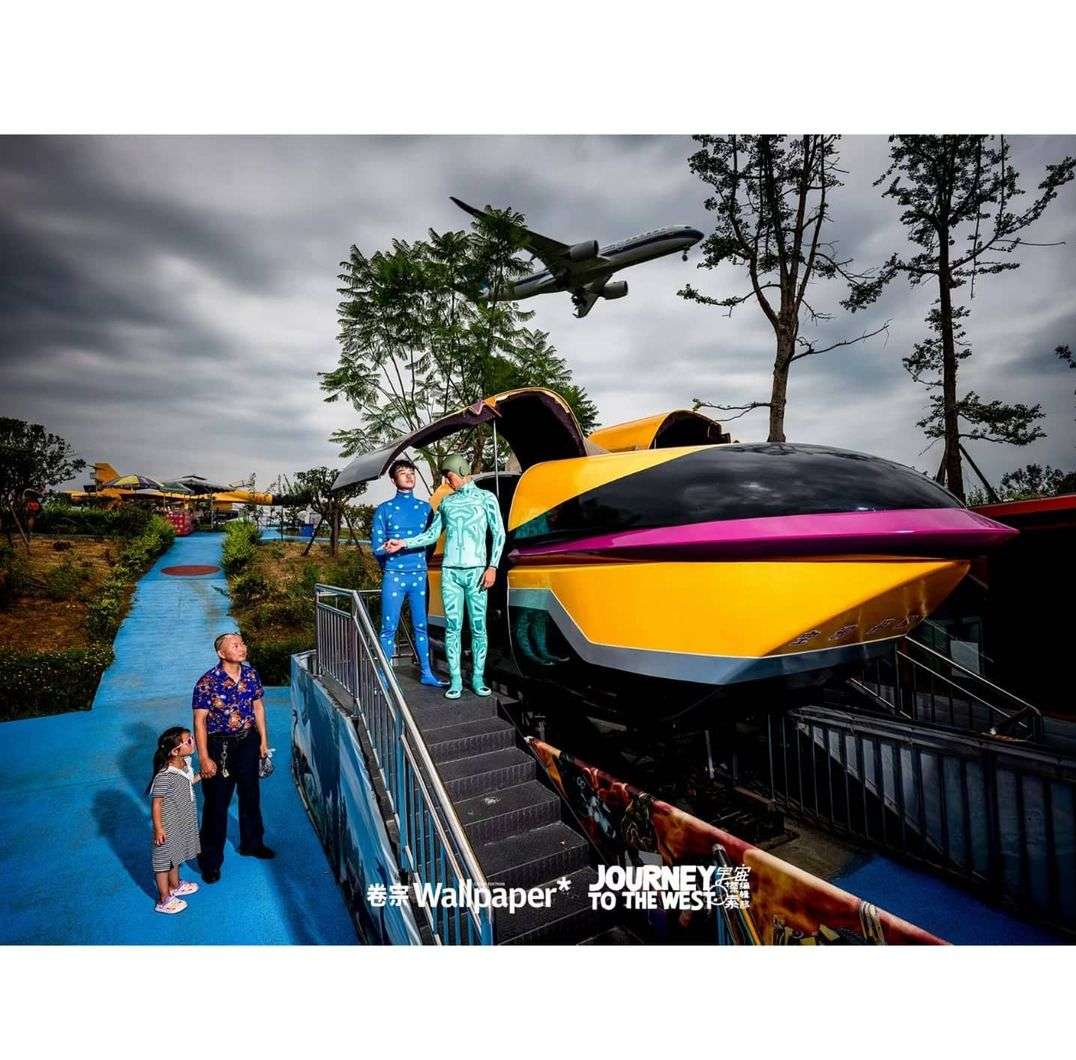People posing near a futuristic train with plane overhead at an amusement park. Family scene with girl, man, and men in costumes.