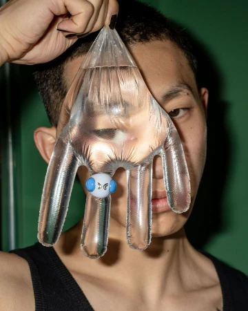 Person with clear hand-shaped water-filled container covering part of face in a portrait-style shot, against a green backdrop.