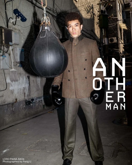 A man wearing boxing gloves and a suit stands in front of a punching bag in an alleyway with exposed pipes and magazine text overlay.