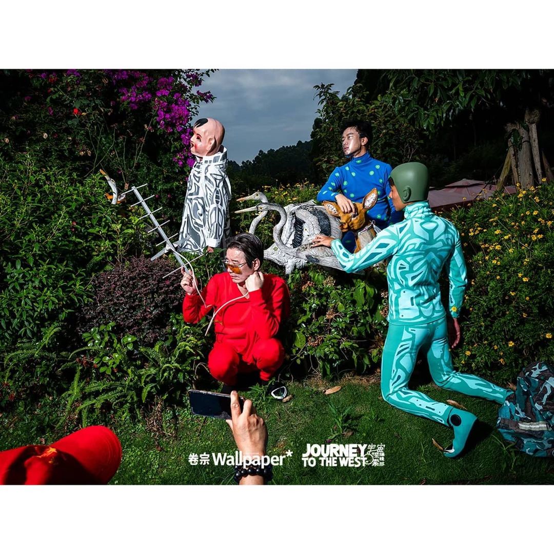 Artistic outdoor scene with four people in unique patterned outfits, surrounded by lush greenery and garden decorations.