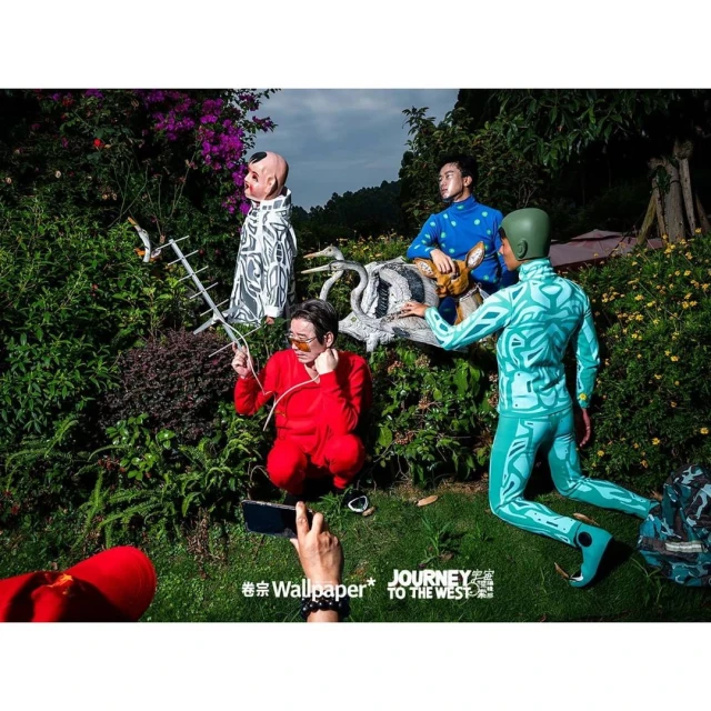 Artistic outdoor scene with four people in unique patterned outfits, surrounded by lush greenery and garden decorations.