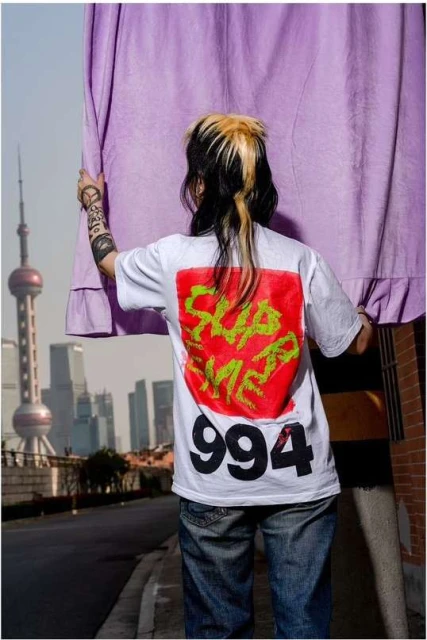 Back view of a person in a Supreme shirt with a city skyline and the Oriental Pearl Tower in the background, partially obscured by a curtain.