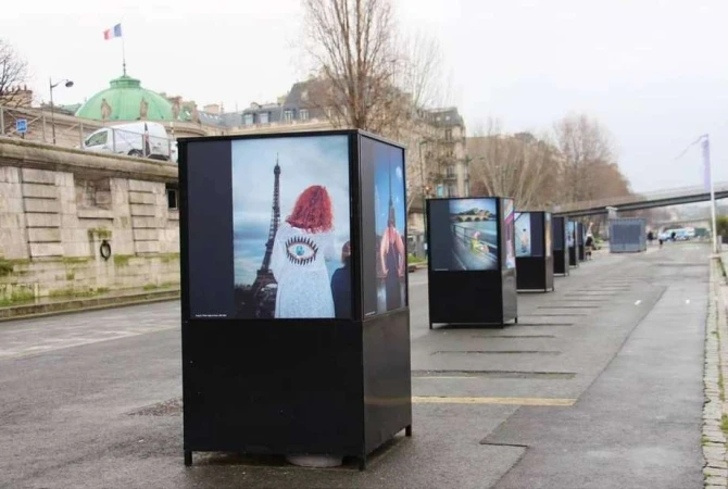 Outdoor art installation in Paris features photos of models with the Eiffel Tower as backdrop on a cloudy day.