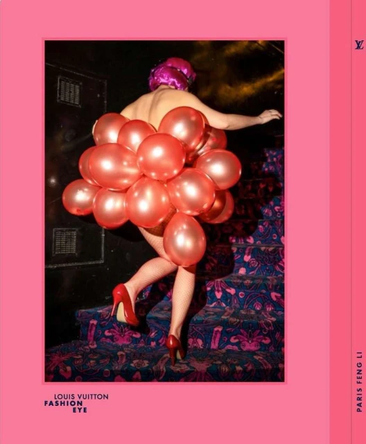 A woman wears a pink head covering and red high heels, adorned with red balloons, walking on a patterned blue staircase against a dark background.