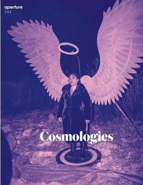 Magazine cover with an adult female standing wearing angel wings, ring light halo, dark coat, and boots in a nighttime outdoor environment.