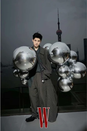 Portrait of a young Asian man in a stylish grey outfit posing with reflective spheres against a Shanghai cityscape backdrop; fashion editorial.