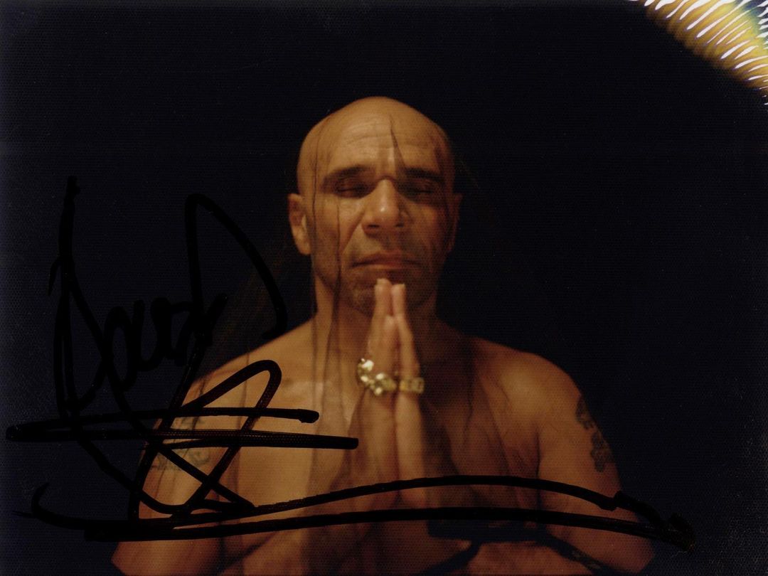 Bald adult male with jewelry, shirtless and praying in a dark studio setting, creating a portrait focused on spirituality and devotion.