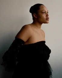 Portrait of a woman wearing a black strapless dress against a plain wall photographed by Fenn O’meally.