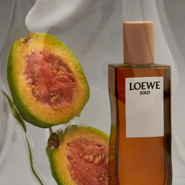 Loewe Solo fragrance bottle with guava fruit halves. Brown liquid perfume in a clear glass bottle with minimalist white label.