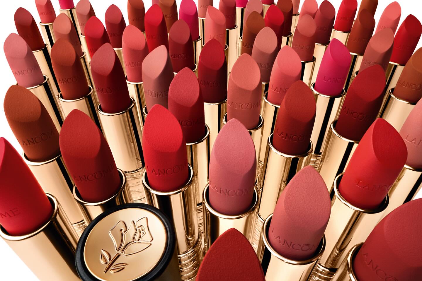 Close-up of numerous red and neutral-toned lipsticks with gold accents arranged closely together in a beauty product display.