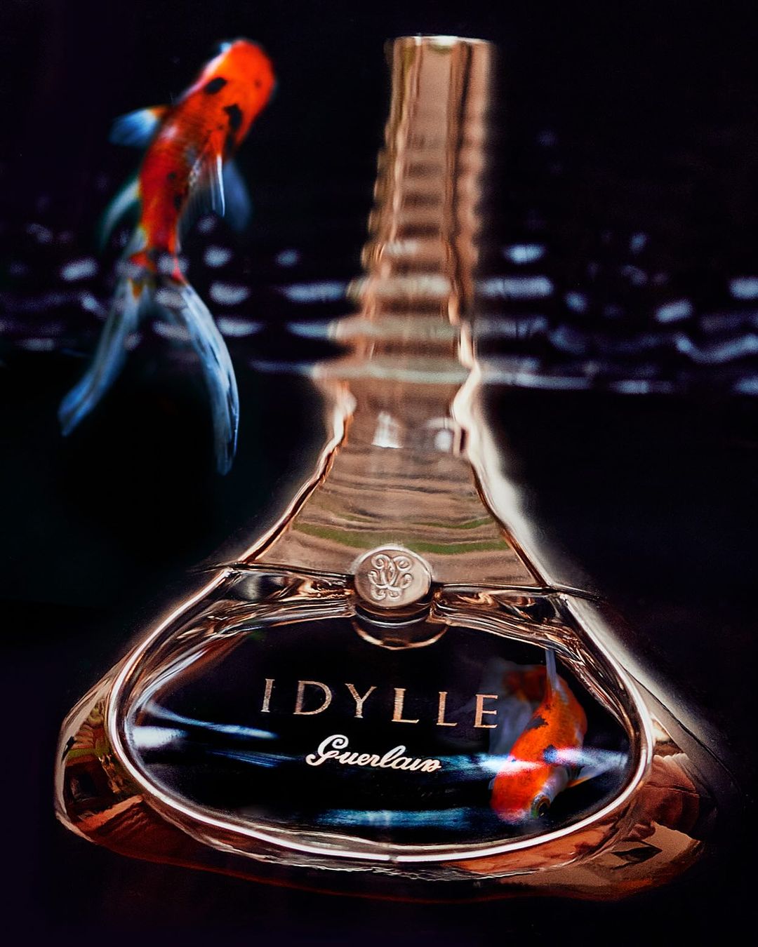 Guerlain Idylle perfume bottle with gold trim reflects light with a koi fish swimming in the background creating a surreal atmosphere.