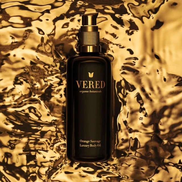 Elegant black VERED Organic Botanicals bottle with gold accents, featuring luxury body oil, set against a textured gold background.